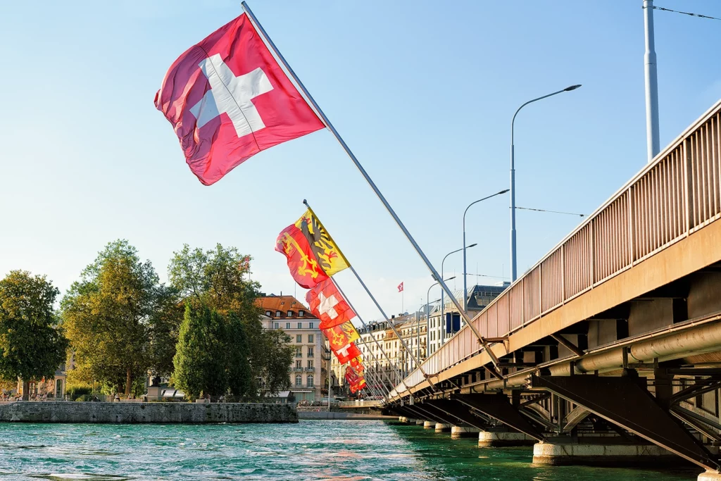 Foto einer Brücke in Genf, auf der eine Reihe von Schweizer und Genfer Kantonsflaggen zu sehen sind – NIMSchweiz hat ein Büro in Genf
